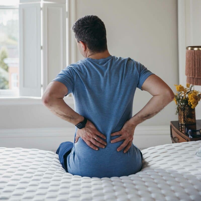 Man sitting on the bed in pain pressing his rubbing his lower back
