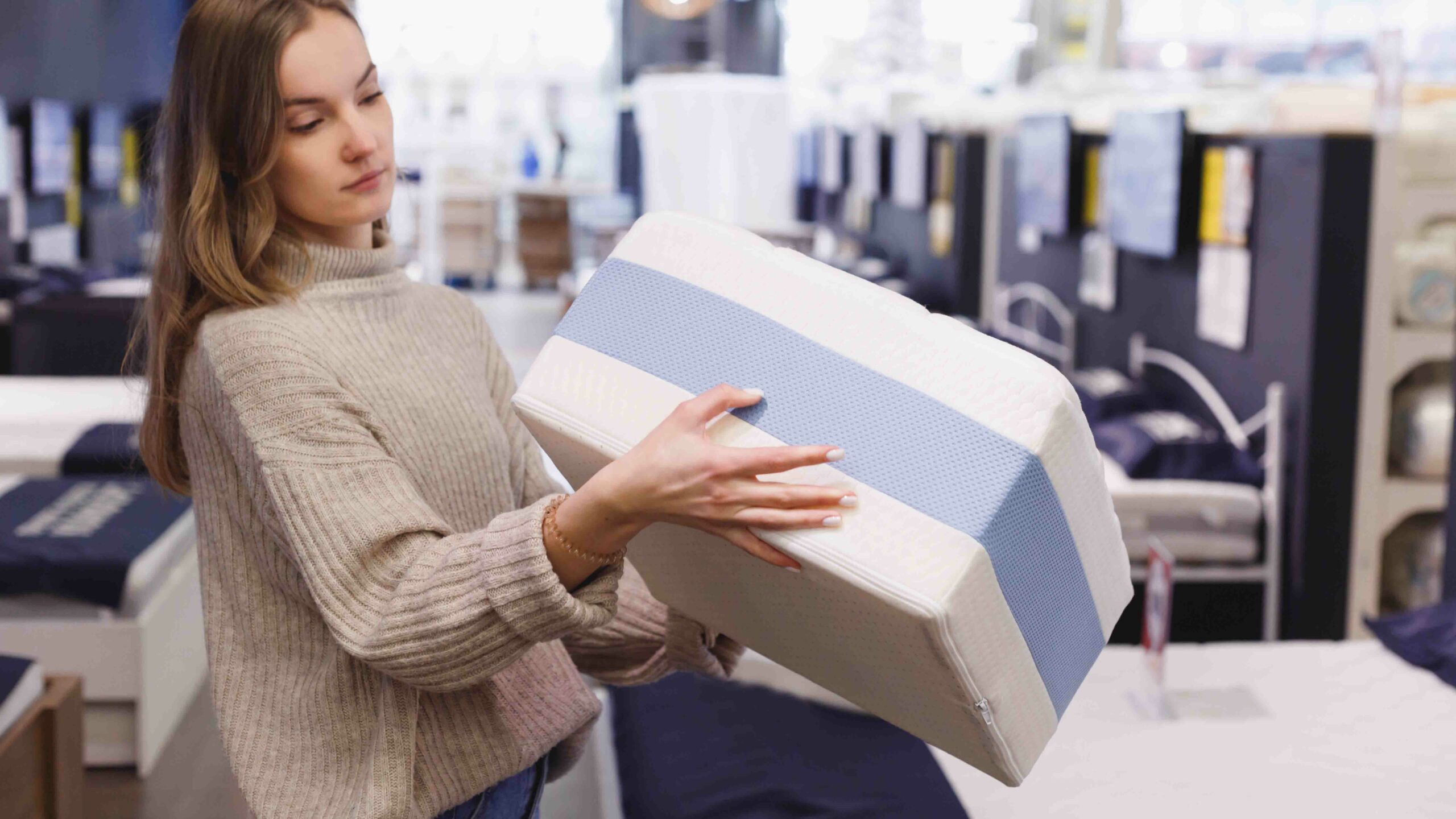 woman holding mattress sample in bed showroom