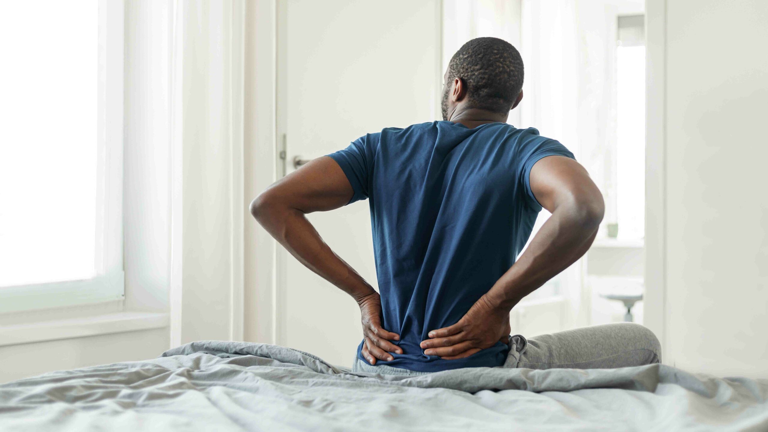 african man having pain touching lower back sitting on bed